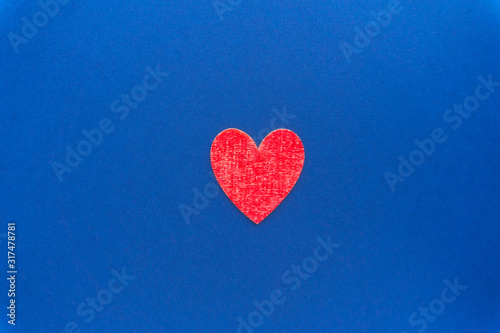 Minimalist valentine background. One red colored wooden heart at classic blue background.
