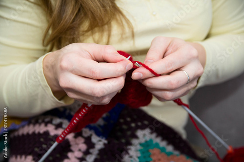 A woman knits on a knitting needlework made of red yarn. Knitting needles in the hands of a woman.