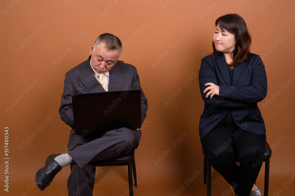Obraz premium Mature Asian businesswoman with mature Asian businessman using laptop