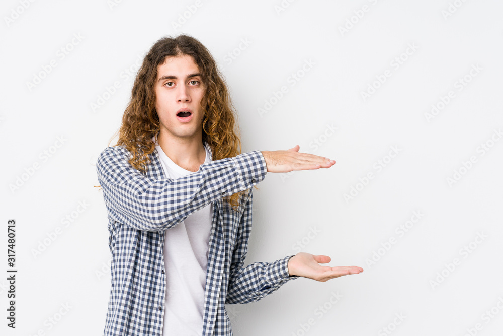 Young long hair man posing isolated shocked and amazed holding a copy space between hands. Young long hair man posing isolated shocked and amazed holding a copy space between hands.