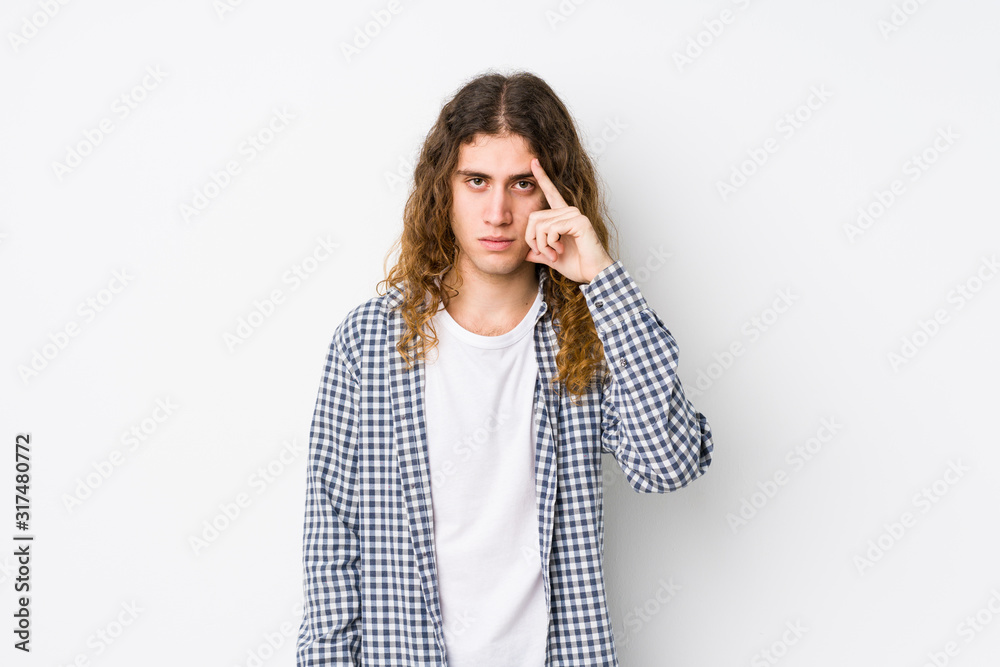 Young long hair man posing isolated pointing temple with finger, thinking, focused on a task. Young long hair man posing isolated pointing temple with finger, thinking, focused on a task.
