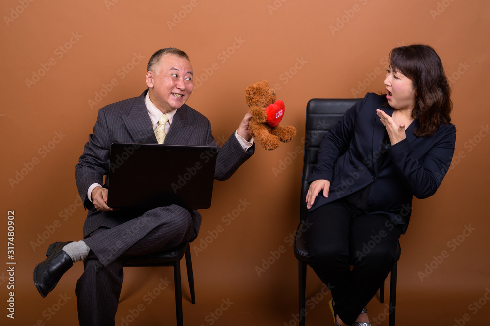 Obraz premium Mature Asian businesswoman with mature Asian businessman using laptop