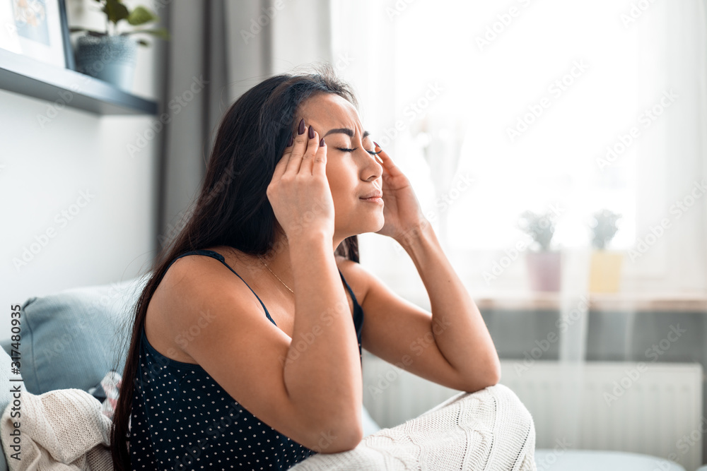 Upset depressed asian girl on couch suffering from headache migraine Upset depressed asian girl on couch suffering from headache migraine