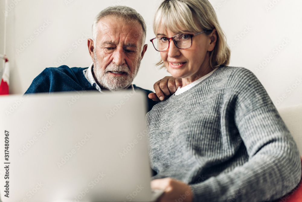 Senior couple relaxing and using laptop computer together sitting on sofa in living room at home.Retirement couple concept Senior couple relaxing and using laptop computer together sitting on sofa in living room at home.Retirement couple concept