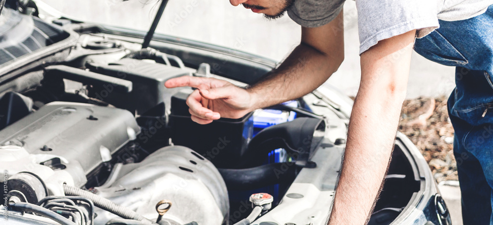 Professional car mechanic in uniform fixing a car engine and repairing checking under the car hood in auto service Professional car mechanic in uniform fixing a car engine and repairing checking under the car hood in auto service