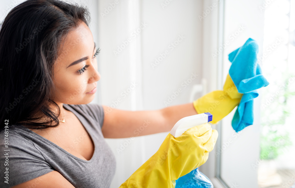 Young asian girl with gloves and spray cleaning windows Young asian girl with gloves and spray cleaning windows