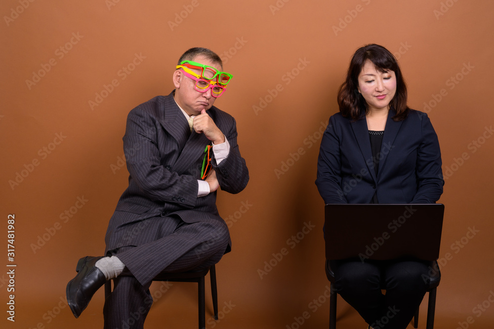 Obraz premium Funny mature Asian businessman with mature Asian businesswoman using laptop
