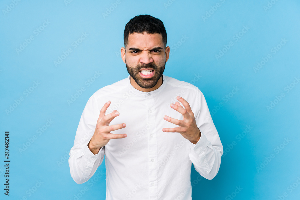 Naklejka premium Young latin man against a blue background isolated upset screaming with tense hands.
