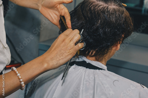Closeup of a hairdresser cuts the wet brown hair of a client in a salon. Hairdresser cuts a woman. Side view of a hand cutting hair with scissors.