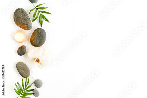 Spa stones, palm leaves, flower white orchid, candle and zen like grey stones on white background. Flat lay, top view