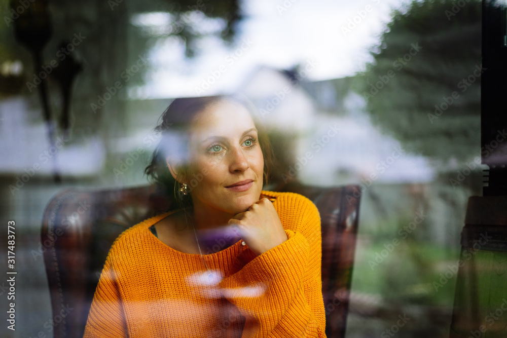© Matthias - Young woman sits in a leather armchair behind a window and looks into the camera