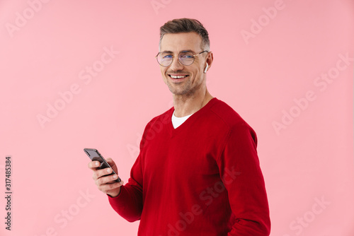 Portrait of handsome man wearing eyeglasses and earbuds holding smartphone