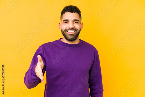 Young mixed race arabic man isolated stretching hand at camera in greeting gesture.