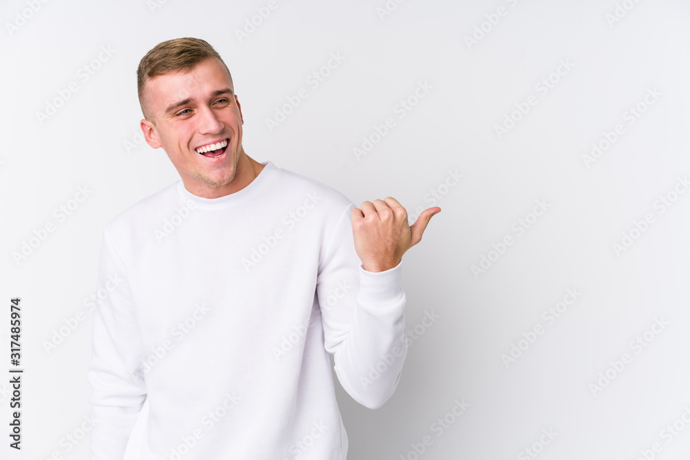 Young caucasian man on white background points with thumb finger away, laughing and carefree. Young caucasian man on white background points with thumb finger away, laughing and carefree.