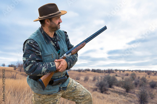 Hunter man in camouflage with a gun during the hunt in search of wild birds or game. Autumn hunting season.