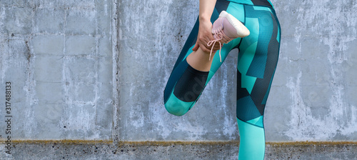 Foto A sporty slim girl in leggings and a top is standing against a concrete wall and performs a set of exercises