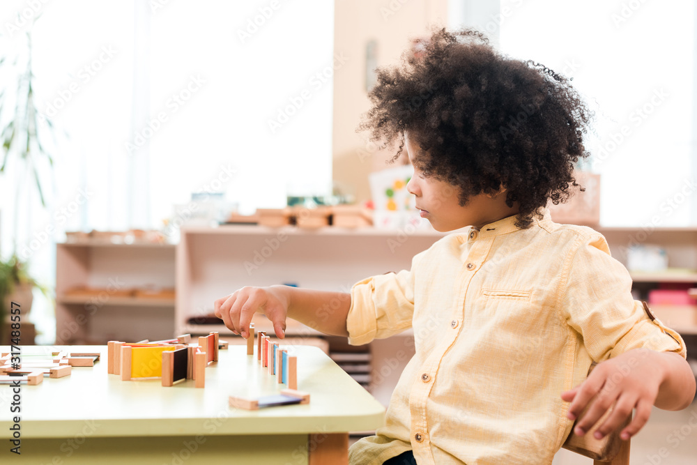 Side view of african american kid playing game at table in montessori school Side view of african american kid playing game at table in montessori school