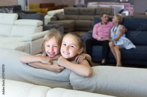 Smiling sisters are standing near new sof