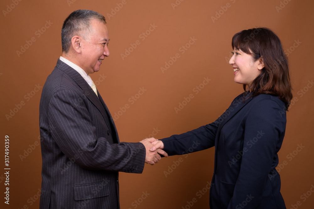 Profile view of happy mature Asian businessman and mature Asian businesswoman shaking hands Profile view of happy mature Asian businessman and mature Asian businesswoman shaking hands