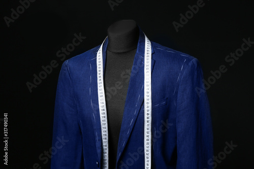 Mannequin with half-finished jacket and measuring tape on dark background