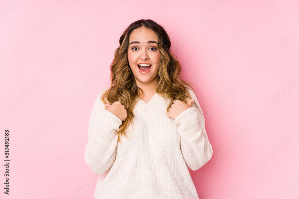 Young curvy woman posing in a pink background isolated surprised pointing with finger, smiling broadly. Young curvy woman posing in a pink background isolated surprised pointing with finger, smiling broadly.