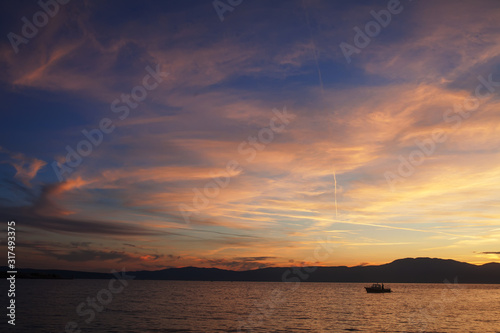 Silhouette of lonely boat in the sunset with dramatic sky. High seas sunset with a fishing ship on the horizon.