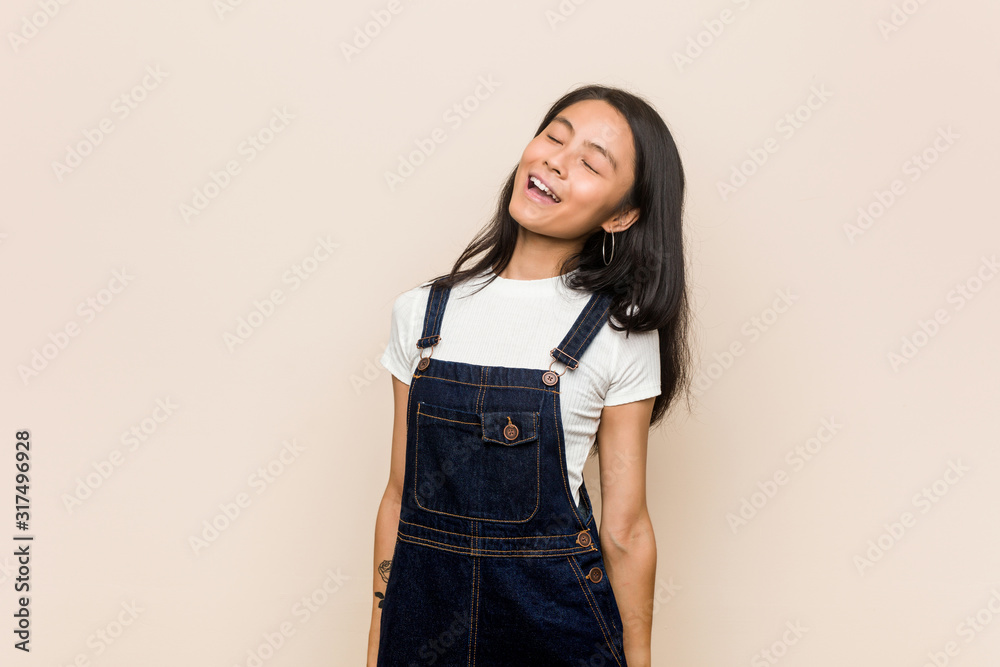 Young cute chinese teenager Young blonde woman wearing a coat against a pink background relaxed and happy laughing, neck stretched showing teeth. Young cute chinese teenager Young blonde woman wearing a coat against a pink background relaxed and happy laughing, neck stretched showing teeth.