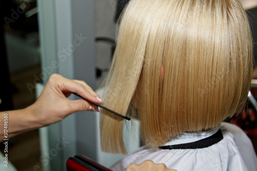 Hairstyle. Attractive blonde with short hair does a hairstyle with an electric iron. Hair straightener gray background. close-up. Macro photo.