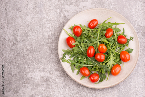 Arugula leaves and cherry tomatoes on a dish standing on a grey textured background