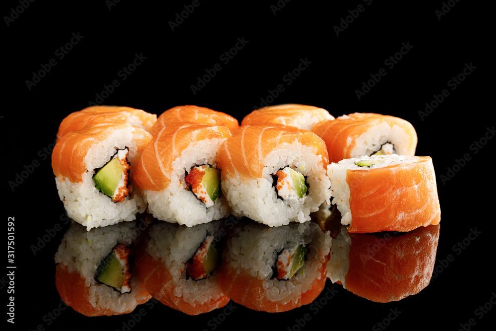 delicious Philadelphia sushi with avocado, creamy cheese, salmon and masago caviar isolated on black with reflection