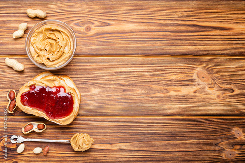 Toast sandwich with peanut butter. Spoon and jar of peanut butter, jam and peanuts for cooking breakfast on a brown wooden background. Creamy peanut paste flat lay with place for text.