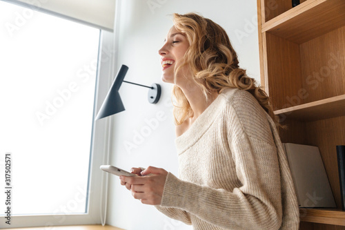 Positive young woman indoors using mobile phone.