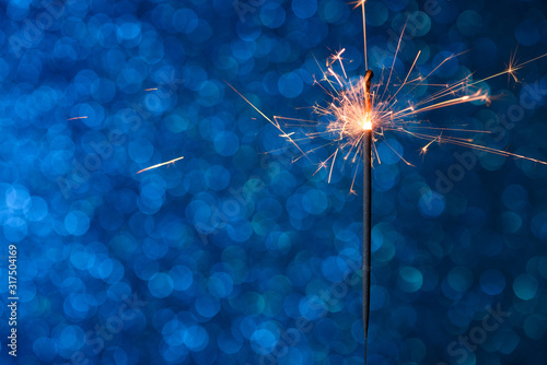 Party sparkler burining over blue bokeh background