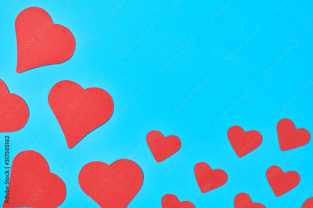 Scattered little and big red paper hearts on blue background. Concept of Valentines Day. Space for text. Top view