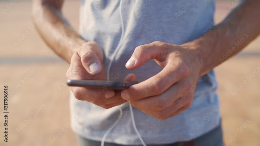 Close up shot of a young male scrolling and typing on his smartphone outdoors on a sunny day Close up shot of a young male scrolling and typing on his smartphone outdoors on a sunny day