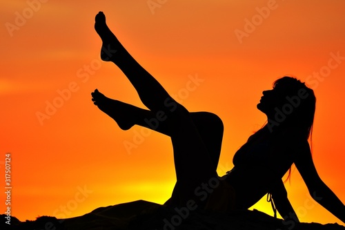Silhouette of slim woman sitting with raised legs at sunset