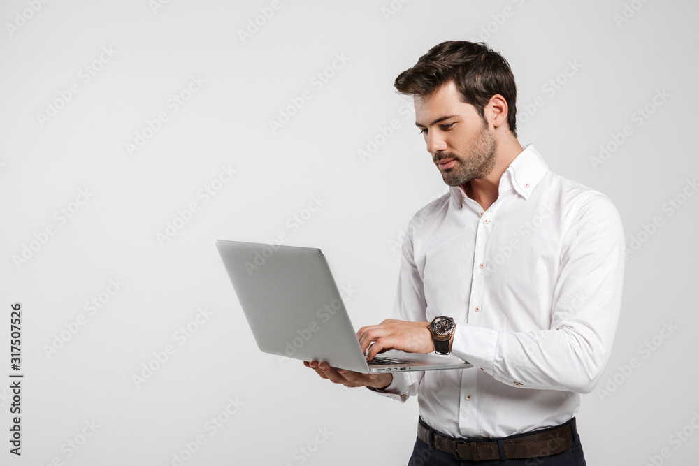 Image of young successful businessman holding and using laptop Image of young successful businessman holding and using laptop