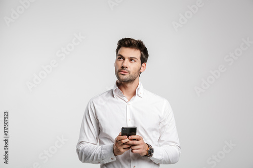 Image of thinking businessman typing on cellphone and looking upward