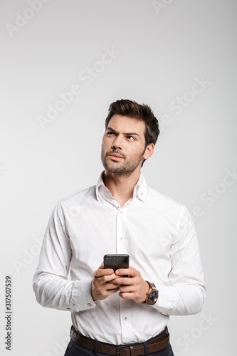 Image of thinking businessman typing on cellphone and looking upward