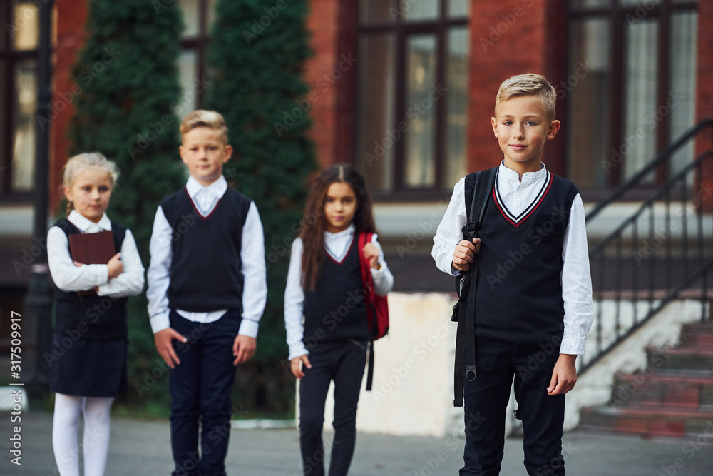 Group of kids in school uniform posing to the camera outdoors together near education building Group of kids in school uniform posing to the camera outdoors together near education building
