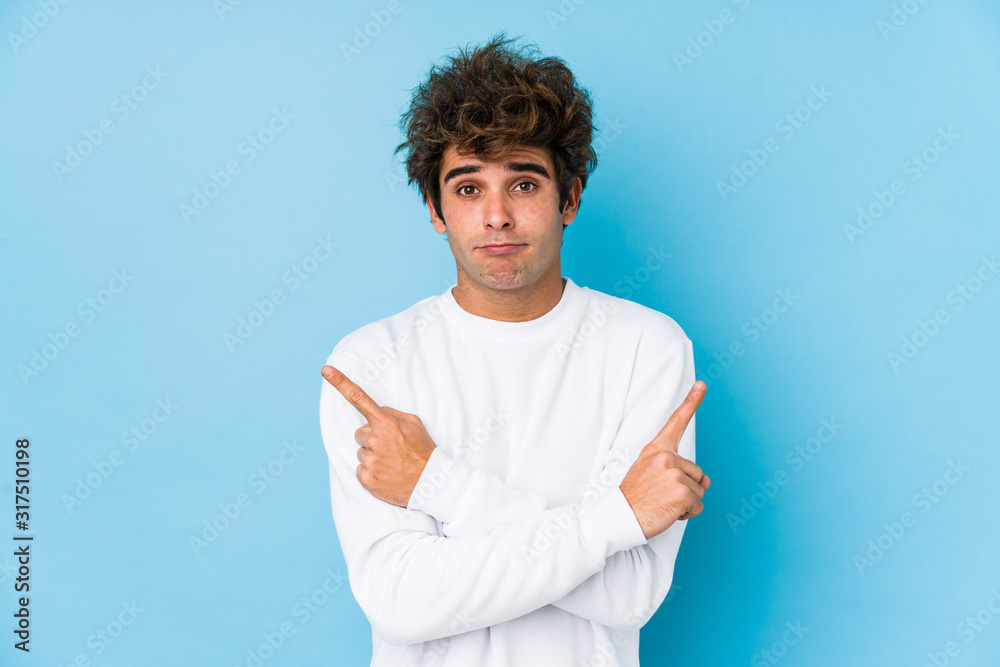 Young caucasian man against a blue background isolated points sideways, is trying to choose between two options. Young caucasian man against a blue background isolated points sideways, is trying to choose between two options.