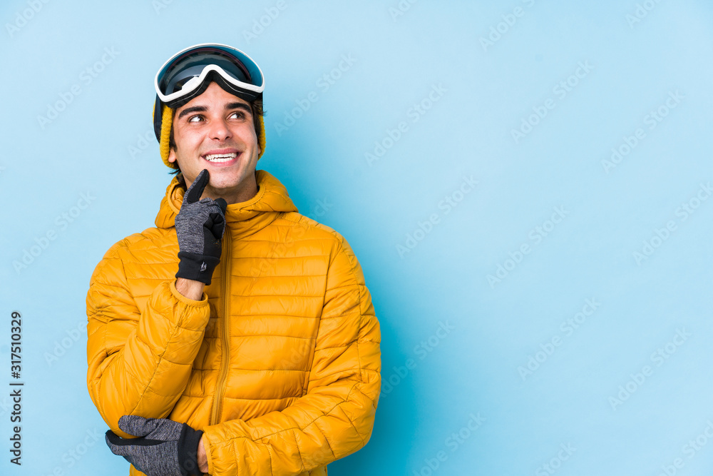 Young skier man wearing snowboard goggles isolated relaxed thinking about something looking at a copy space. Young skier man wearing snowboard goggles isolated relaxed thinking about something looking at a copy space.