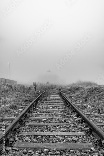 Railway in the fog. Train tracks disappear into strange glowing fog. Black white photo.