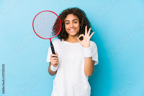 Young african american woman playing badminton cheerful and confident showing ok gesture. © Asier