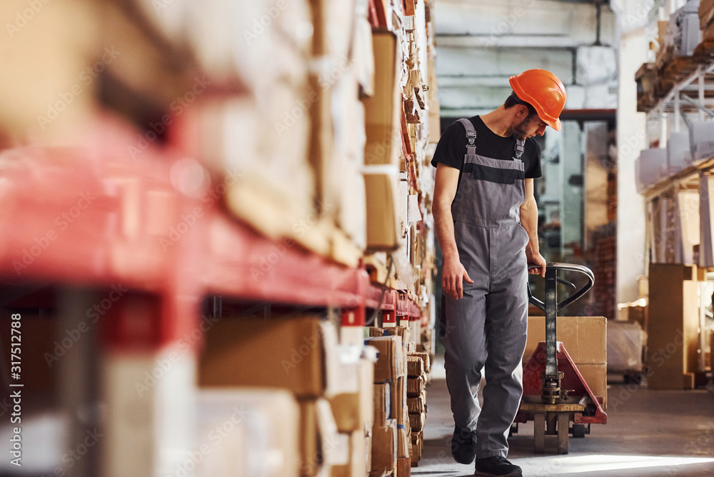 Young male worker in uniform is in the warehouse pushing pallet truck Young male worker in uniform is in the warehouse pushing pallet truck