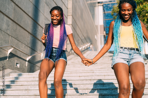 Two beautiful young black sisters walking downstairs together holding hands