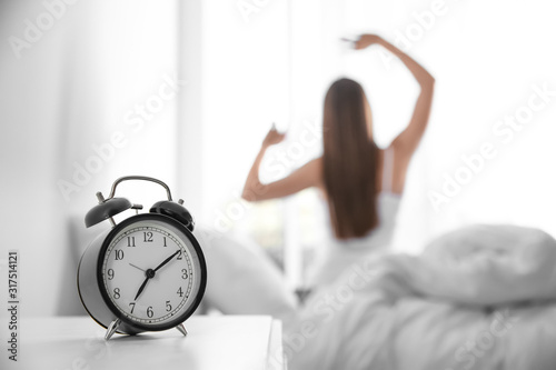 Young woman stretching at home in morning, focus on alarm clock