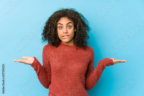 Young african american curly hair woman confused and doubtful shrugging shoulders to hold a copy space.