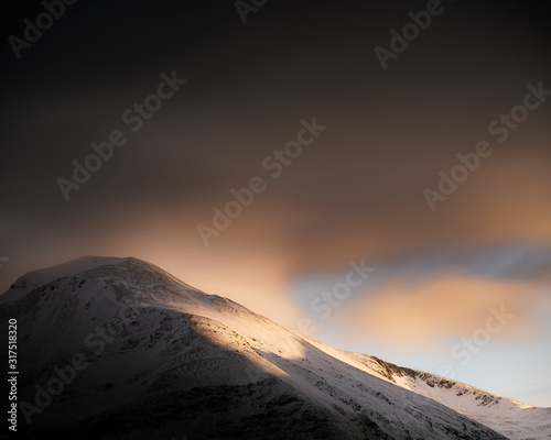 Dramatic clouds and golden sunshine on snowy Ben Nevis - UK's highest mountain