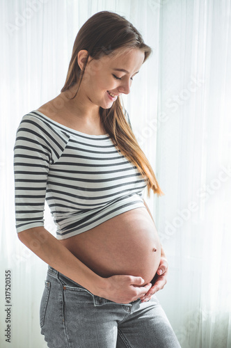 Happy pregnant woman with big belly by the window. Concepts of pregnancy and family